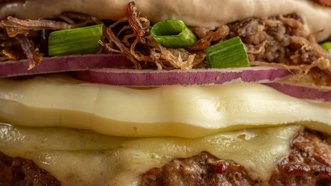 Hambúrguer com costela desfiada e queijo derretido, servido por um parceiro